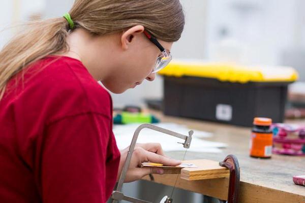 Female undergraduate student sawing metal in a jewelry class.