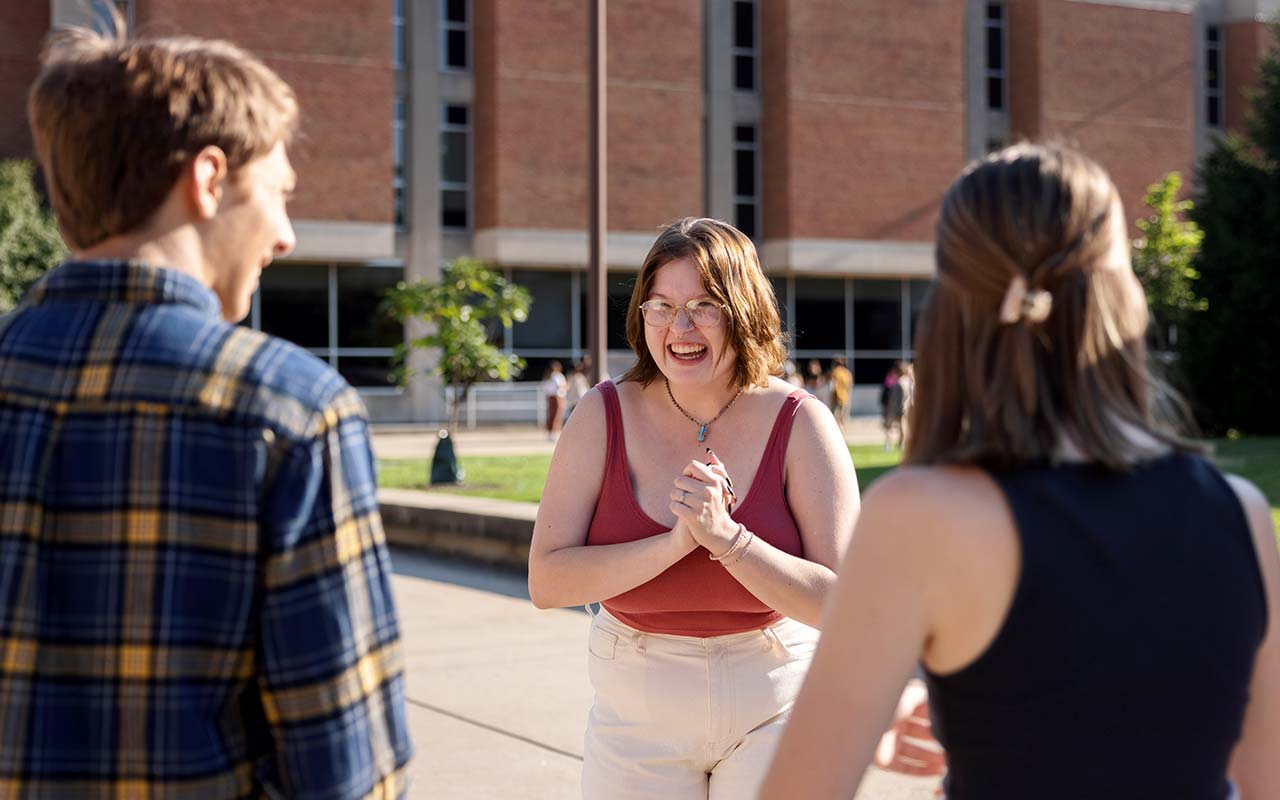 A female student at IU Indianapolis faces two other students and laughs as they all talk.